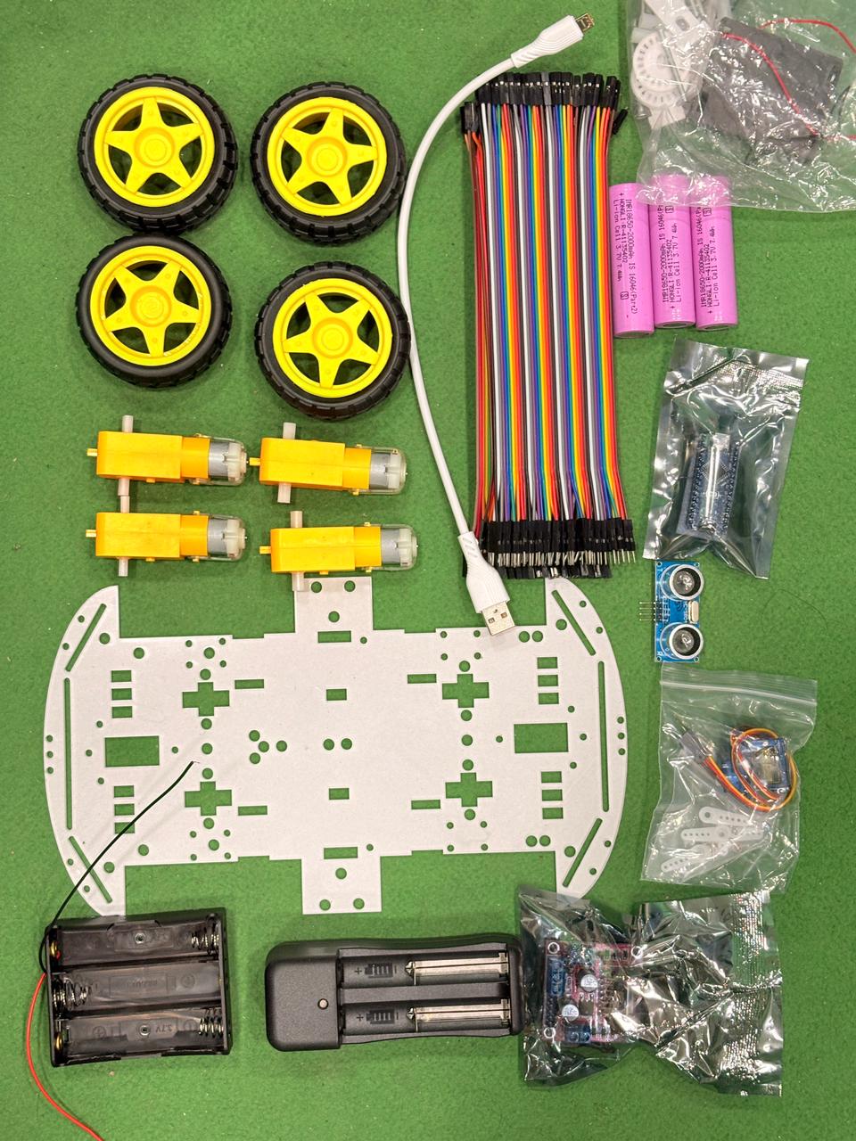 Robotics kit components including wheels, connectors, and battery pack on a green background